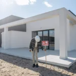 Top AI Tools for Real Estate Agents to Generate Leads and Close Deals Faster Real estate agent with hard hat standing by a modern house for sale.