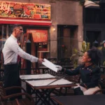 7 AI Tools for Small Restaurant Owners to Automate Marketing and Cut Costs A waiter serves a menu to a seated customer at an outdoor restaurant with colorful signage.
