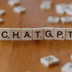 Scrabble tiles spelling "CHATGPT" on wooden surface, emphasizing AI language models.
