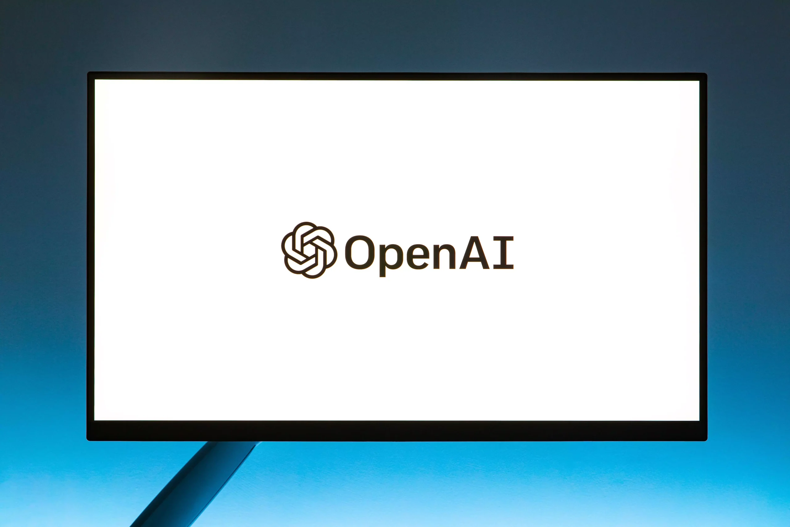 Minimalistic display of OpenAI logo on a monitor with a gradient blue background, representing modern technology.